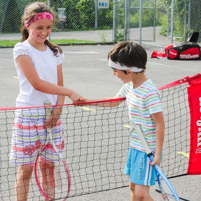 A girl and a boy who plays tennis in an outdoor tennis court shaking hands after a match