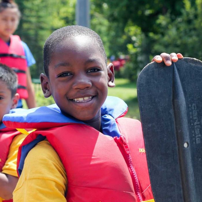 Two boys looking at the camera wearing life vest and holding a water paddle
