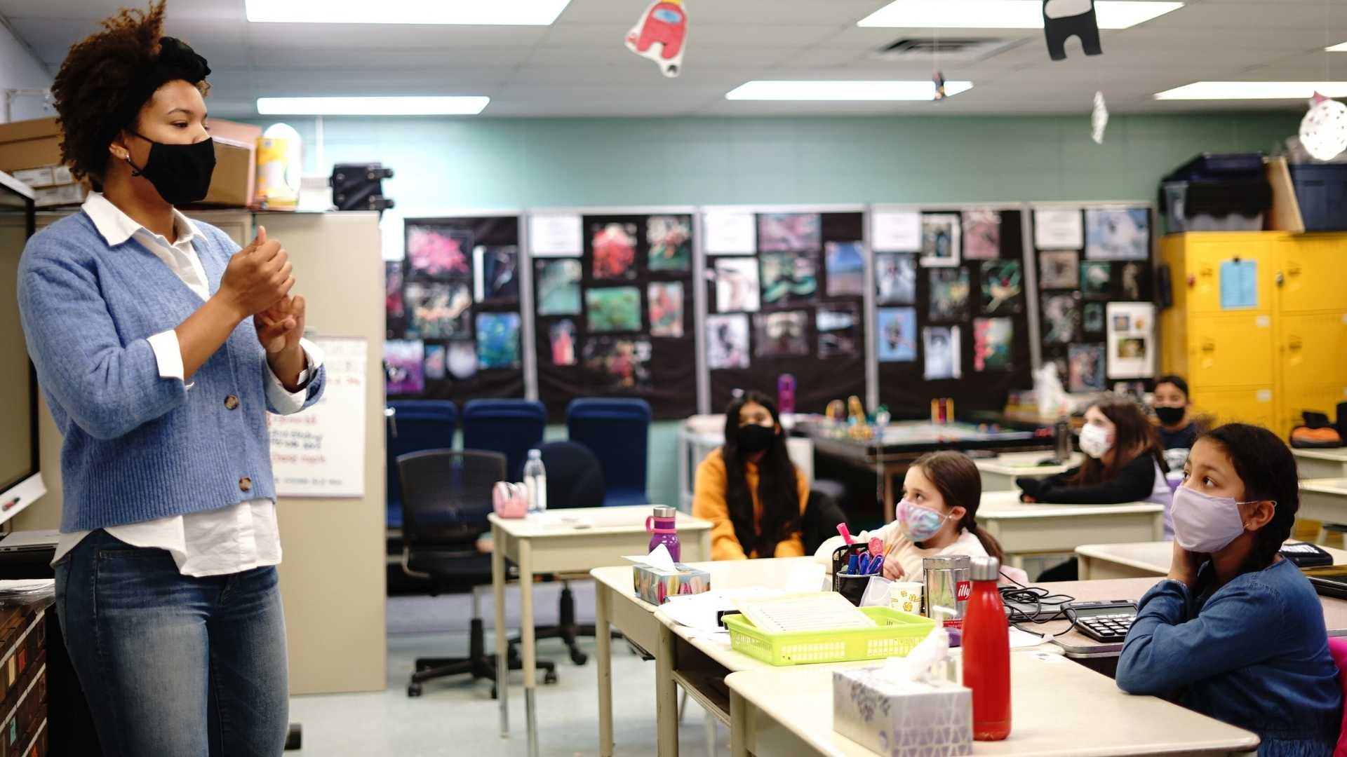 A standing woman with a face mask speaking in front of a class