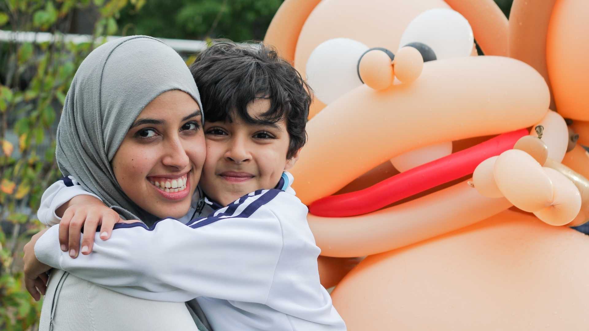 A woman and a boy hugging each other at the park with the PEYO mascot