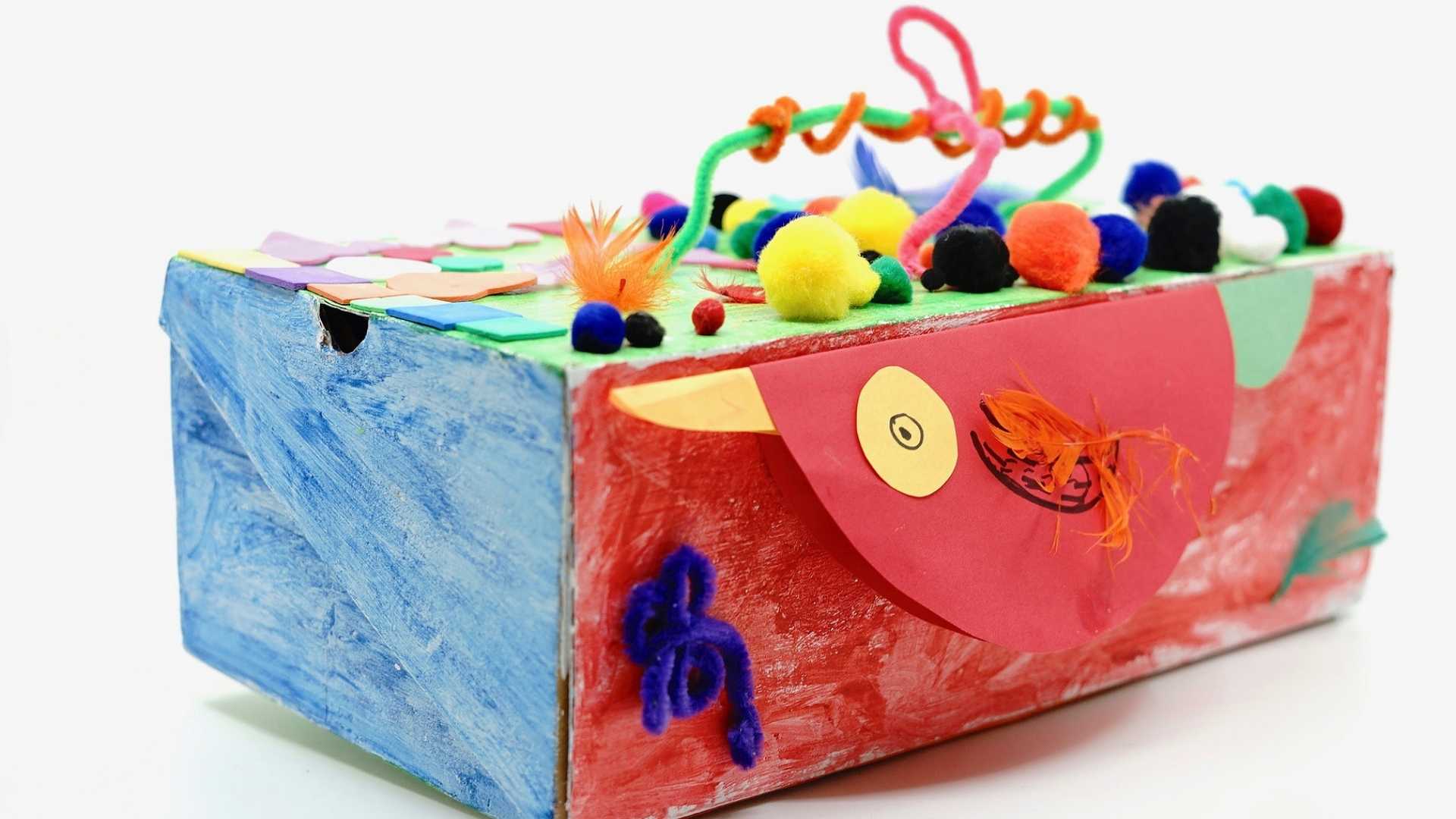 A decorated box with colorful pipe cleaners, feather, foams and pompom cotton balls
