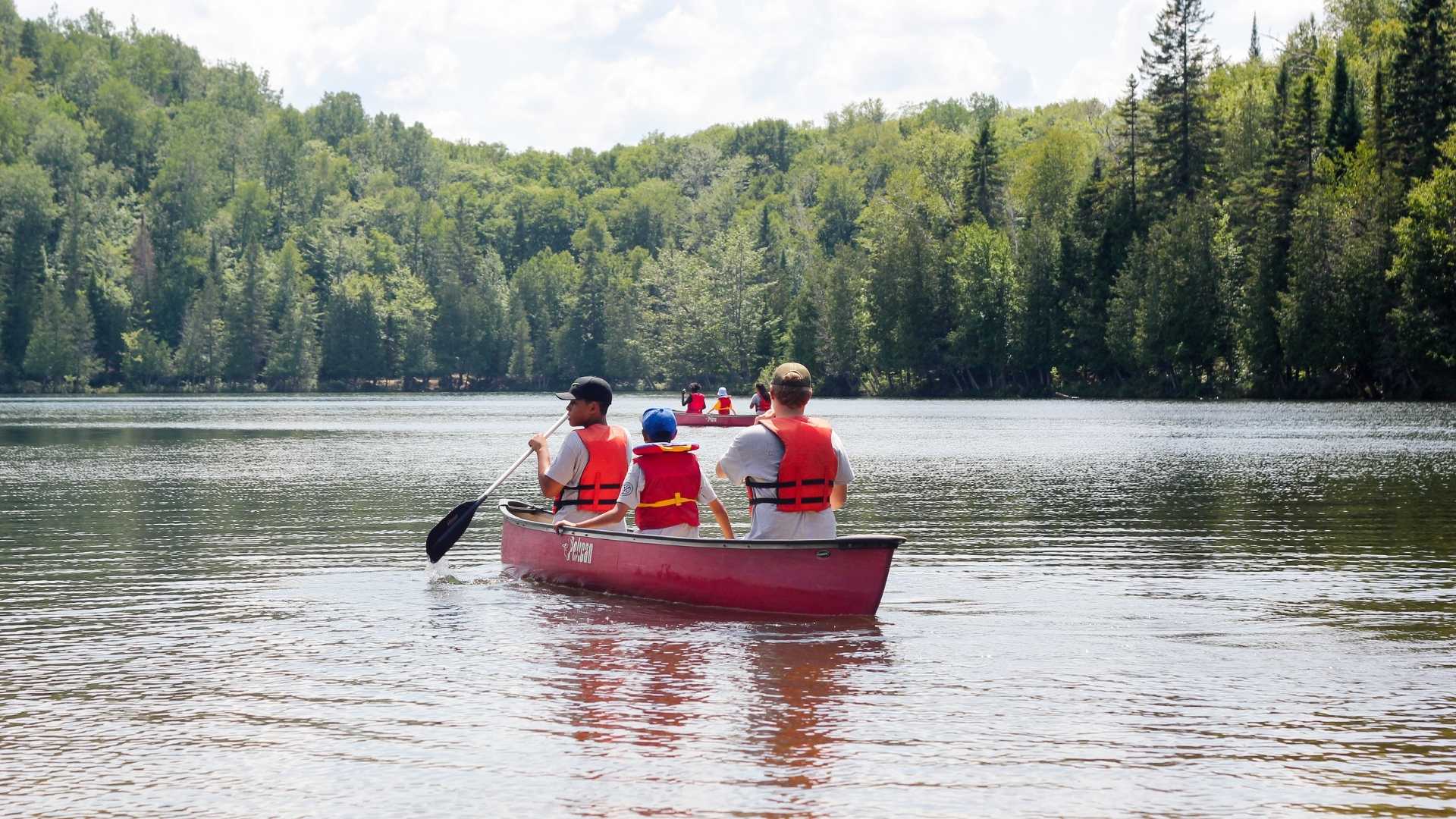 A group of people riding a boat while doing some water exploration in a lake that is surrounded by beautiful trees