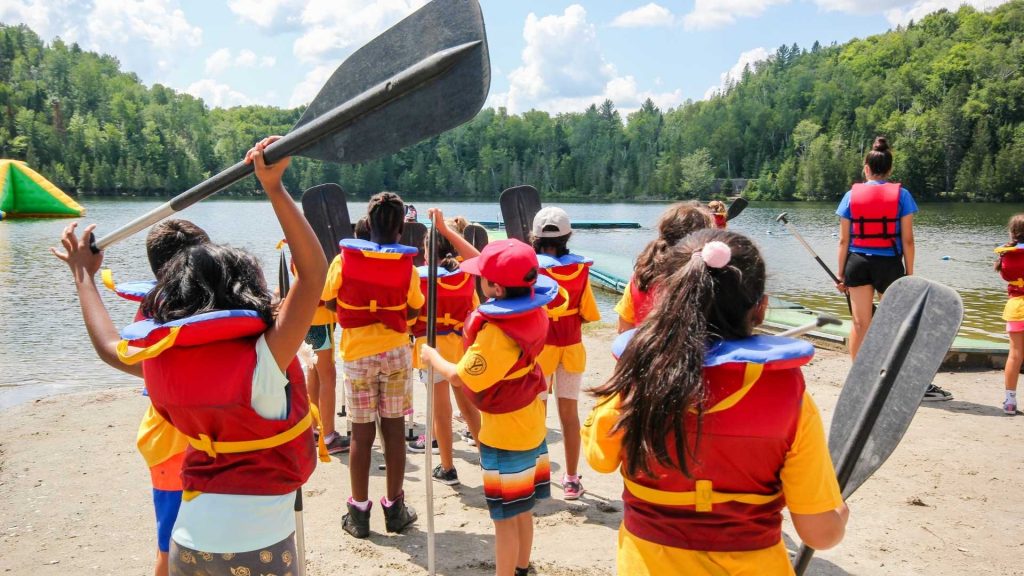 A group of kids wearing life vest while holding their water paddles, ready to do water exploration