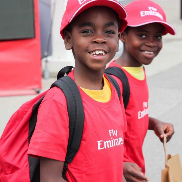 Two boys looking at the camera wearing a "Fly Emirates" cap and shirt